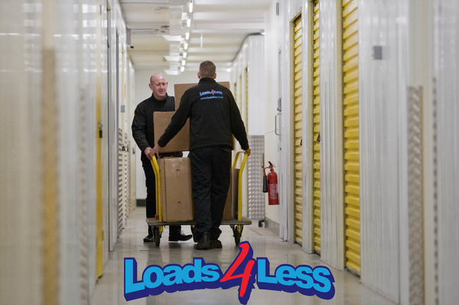 Image of two Loads4Less employees using a trolley to take boxes down to storage unit for customer in Norwich.