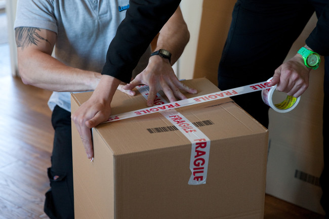 Image of Loads4Less employee taping a cardboard box. This being for Loads4Less packing service.
