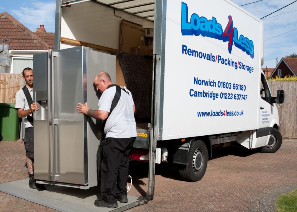 Two loads4less employees using straps to lift and move a double American style fridge.